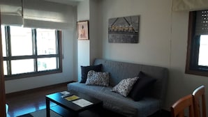 A living room with a grey sofa, two pillows, a coffee table with papers, and a painting on the wall.