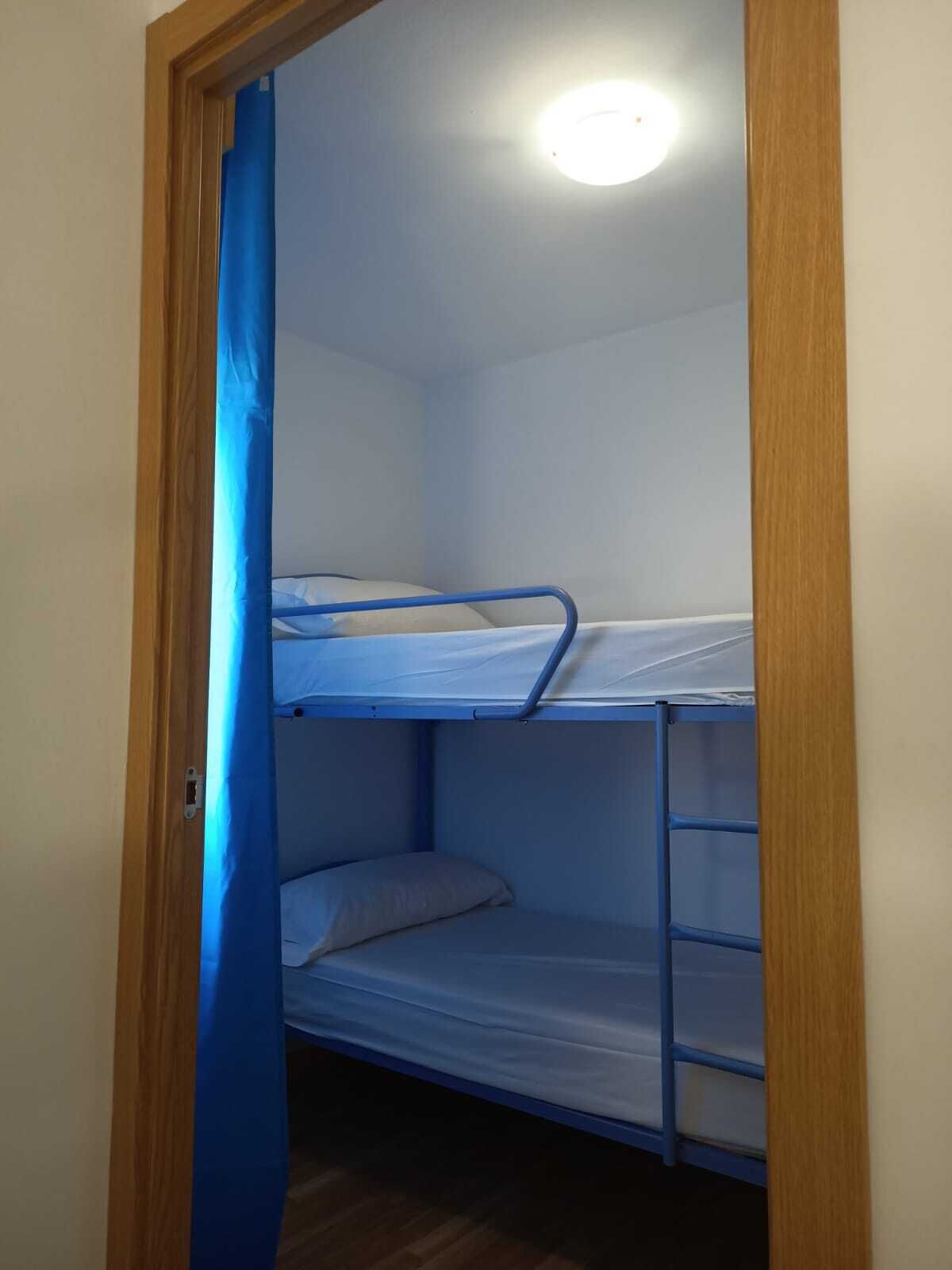Une chambre avec un lit superposé, une porte en bois et un luminaire au plafond.