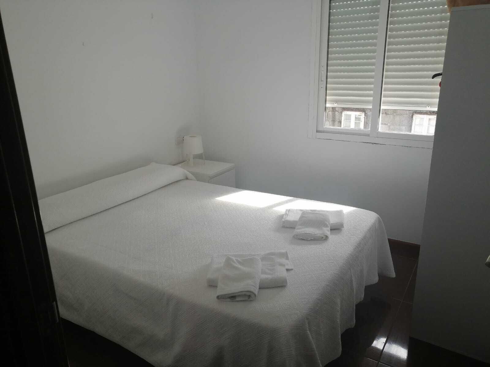 Una habitación pequeña y limpia con una cama individual, una mesita de noche, una ventana con persianas y una toalla sobre la cama.