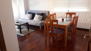 A living room with a sofa, a glass-top dining table with chairs, and a wooden floor.