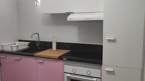 A kitchen with white cabinets, a black countertop, a sink, a wooden cutting board, a gas stove, and a built-in oven.