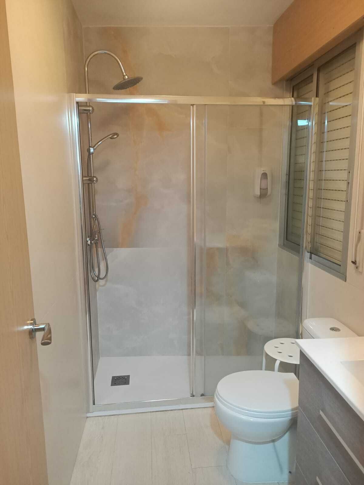 Een moderne badkamer met een douchecabine van glas, een wit toilet en een klein, wit krukje.