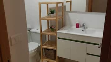 Un baño con un estante de madera, un inodoro, un lavamanos con espejo y una franja verde en la encimera.