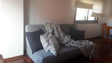 Un sofá gris con almohadones estampados y una manta, ubicado cerca de una ventana con vistas al exterior.