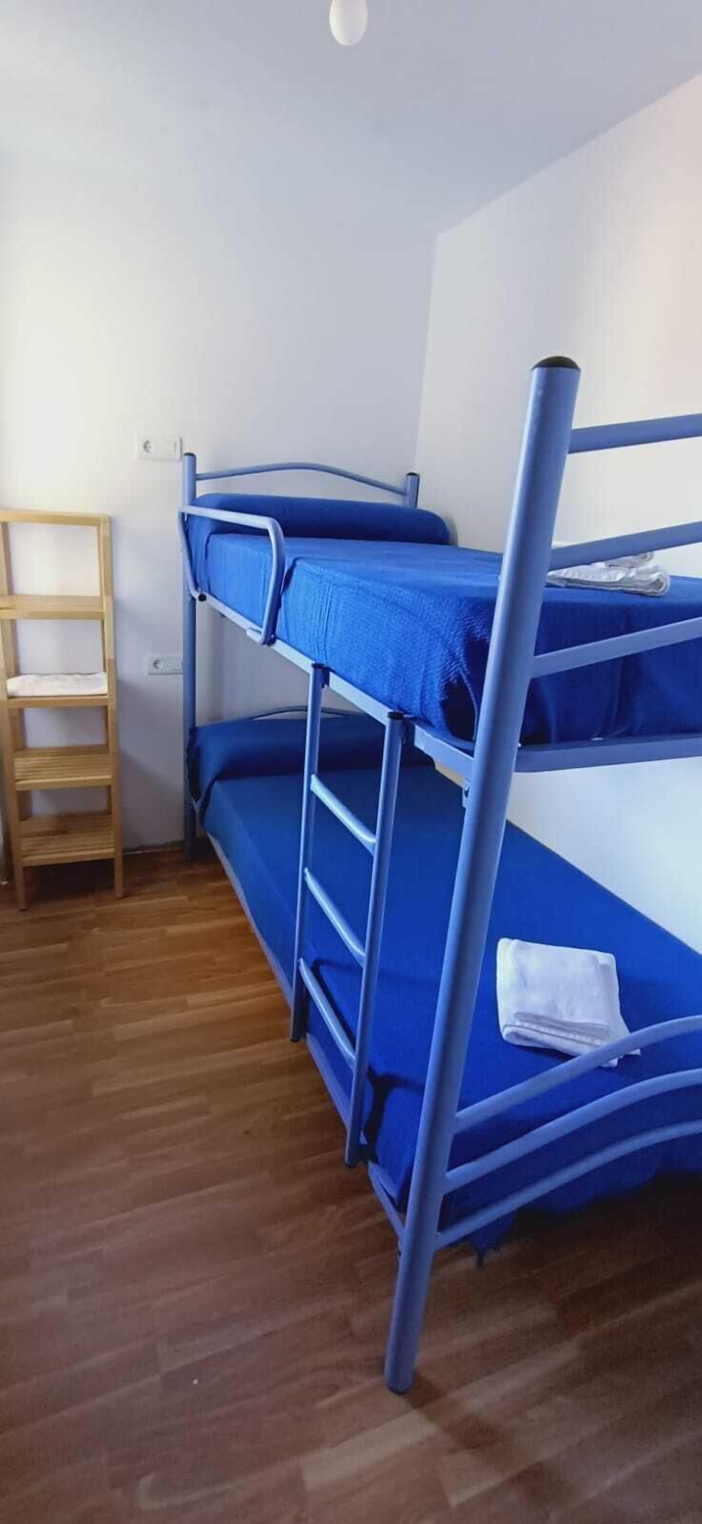 A bunk bed with a blue mattress and metal frame, a wooden ladder, and a white towel on the lower bunk.