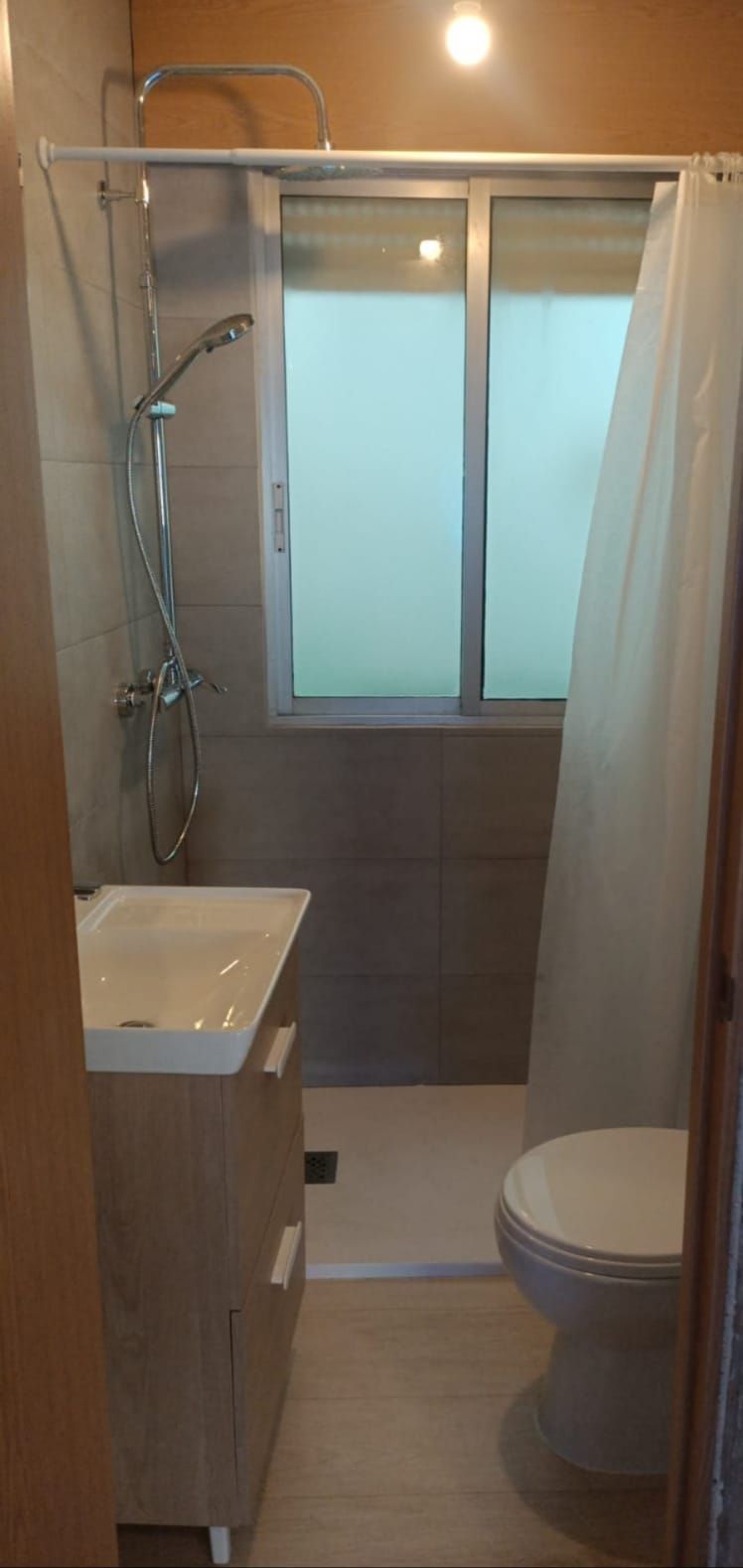 A small, modern bathroom with a shower, toilet, and sink.