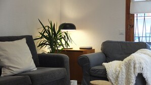 A living room with a grey sofa, a small wooden table with a white mug, a grey armchair with a white throw, and a large plant under a lamp. - Beach Apartment Entre Pinos P1 (Torredembarra)