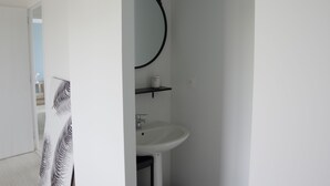 Un baño con un lavamanos blanco, un toallero negro y un recipiente blanco sobre una repisa.