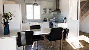 Una cocina moderna con armarios blancos, encimera de mármol, taburetes negros y un ventanal grande.