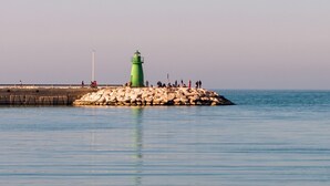 A calm sea with a rocky pier and a green lighthouse.