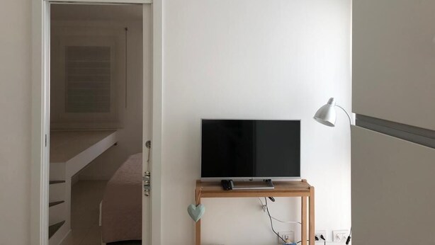 A bedroom with a bed, a TV on a stand, a bedside table, and a lamp.