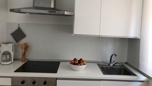 A modern kitchen with a black countertop, a white bowl of fruit, a coffee maker, and a stainless steel range hood.
