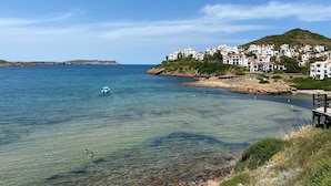 Un pueblo costero con aguas cristalinas, un litoral rocoso y edificios blancos con tejados rojos.