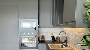 Een moderne keuken met grijze kastjes, een inbouwoven, een roestvrijstalen spoelbak en een gasfornuis.