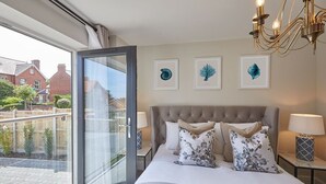 A bedroom with a large bed, a glass door leading to a balcony, and three framed botanical prints on the wall. - Host & Stay | The Hampton at Prospect Hill Apartments (Whitby)
