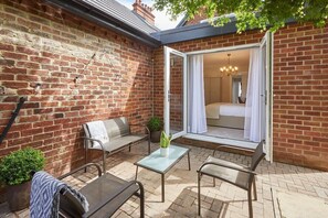 A cozy patio area with a brick wall, a glass door leading to a bedroom, and outdoor seating.
