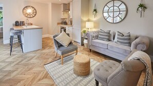 A modern living room with a grey sofa, a small round ottoman, and a herringbone wood floor. - Host & Stay | The Hampton at Prospect Hill Apartments (Whitby)