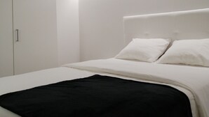 Ein modernes Schlafzimmer mit Bett, weißen Wänden und einer Deckenleuchte.