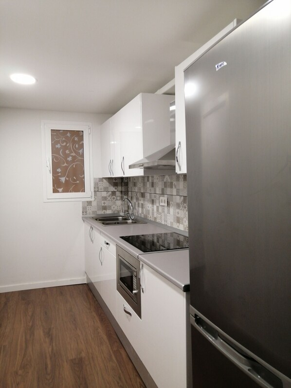 A modern kitchen with white cabinets, a stainless steel refrigerator, a microwave, and a sink.