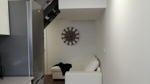 Eine kleine Küche mit einem Kühlschrank, einem weißen Sofa und einer Wanduhr.