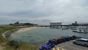 Un puerto marítimo costero con barcos amarrados, una torre de salvavidas y un edificio con la leyenda 'SAUVETAGE EN MER'.