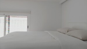 Un dormitorio minimalista con una cama grande, paredes blancas y un ventanal corredero que da a un espacio exterior.