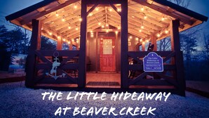 En stuga av trä med ljusslingor, med skylten ”Det lilla gömstället vid Beaver Creek”.