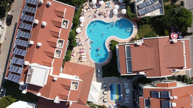 An aerial view of a hotel with a central swimming pool surrounded by sun loungers and umbrellas, solar panels on the rooftops, and a mix of red-tiled roofs and white walls. - Verona Apart Hotel (Marmaris)
