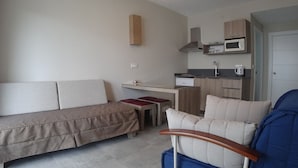 A compact living space with a sofa, a small table, a kitchenette, and a chair. - Verona Apart Hotel (Marmaris)