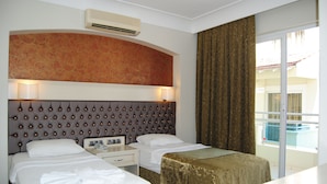 A hotel room with two beds, a large tufted headboard, a minibar, and a view of a pool through a sliding glass door. - Verona Apart Hotel (Marmaris)