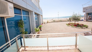A building with large windows overlooking a paved area with potted plants and a view of the beach. - Hotel Kojku (Durrës)