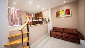 A staircase with wooden steps and a metal railing leading to a bedroom. A brown sofa is positioned in the living area, and a painting is displayed on the wall. - Hotel Kojku (Durrës)