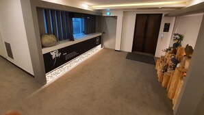 A modern hallway with a reception desk, a wooden sculpture display, and a door with an elevator. - Owl Hotel (Sacheon)