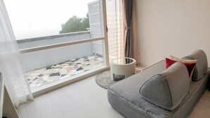 A balcony with a tiled floor, a grey sofa with cushions, and a white lamp. - Owl Hotel (Sacheon)