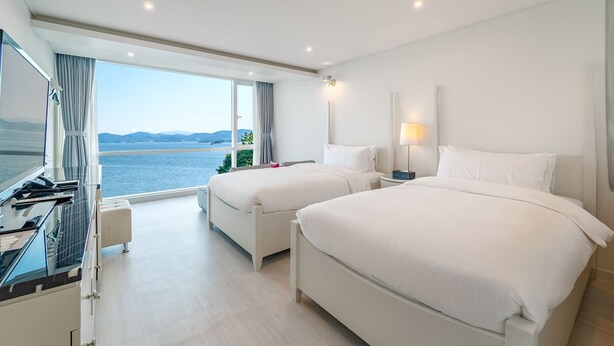A hotel room with two beds, a desk, and a view of the sea. - Owl Hotel (Sacheon)