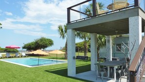 Un espace piscine doté d’un coin salon abrité, d’une table et de chaises.