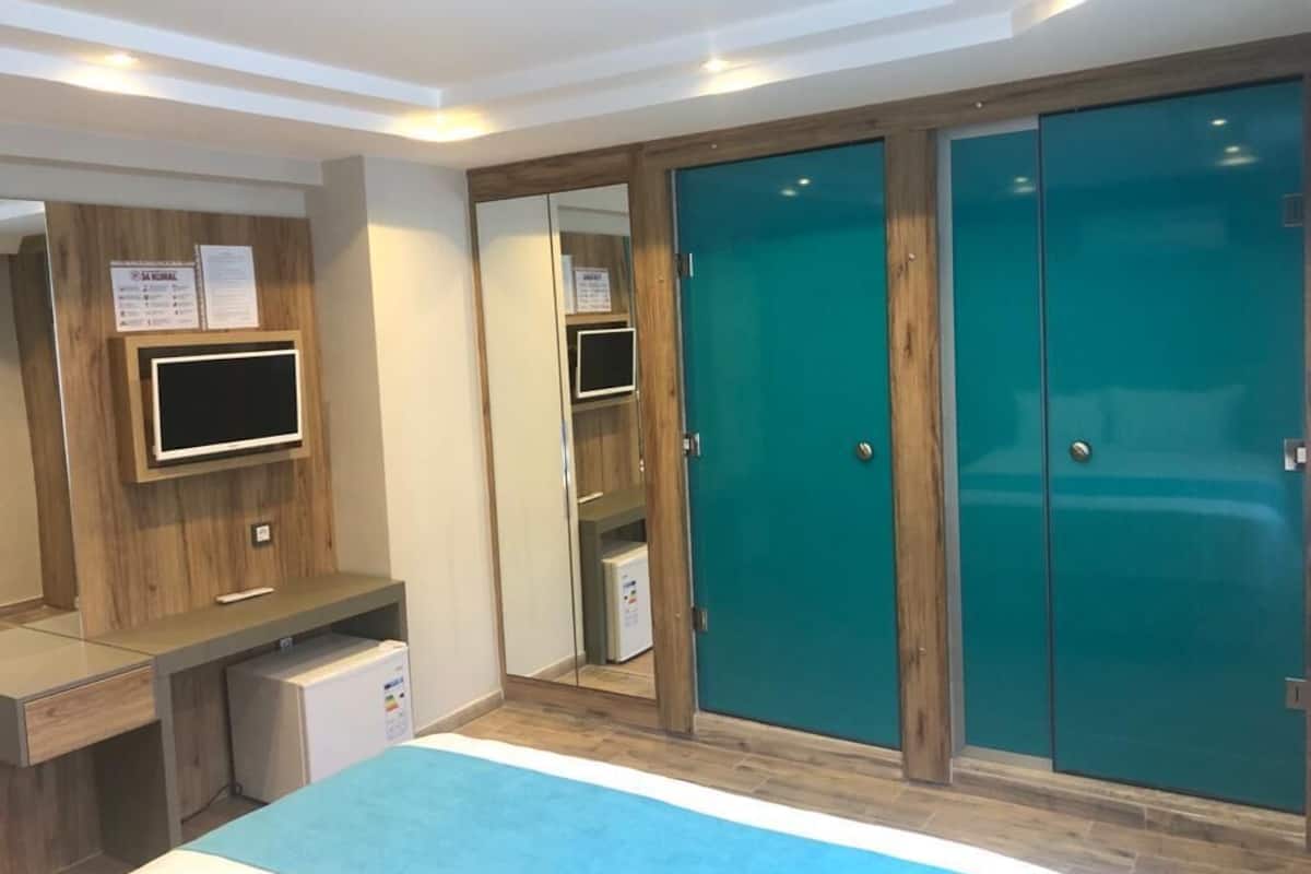 Habitación de hotel con cama, televisor montado en la pared, escritorio con computadora y armario de dos puertas.