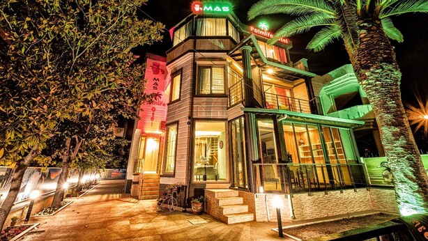 Un hotel con diseño moderno, que presenta un llamativo letrero 'MAS' y una palmera en primer plano.