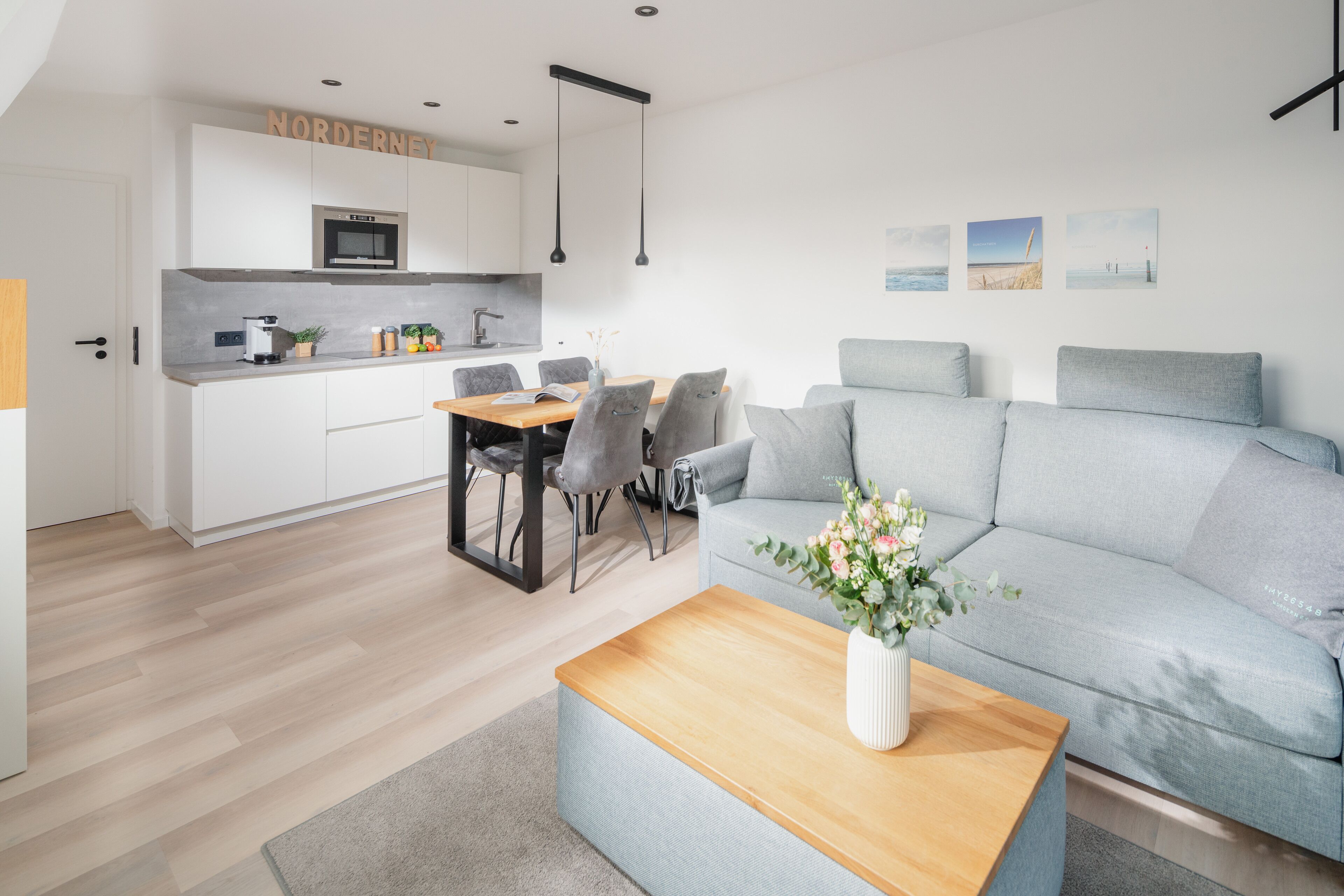 A modern living room with a grey sofa, a wooden coffee table, and a dining area with a table and chairs.
