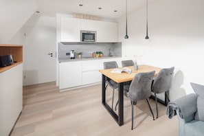 A modern kitchen with white cabinets, a wooden dining table, and grey upholstered chairs.