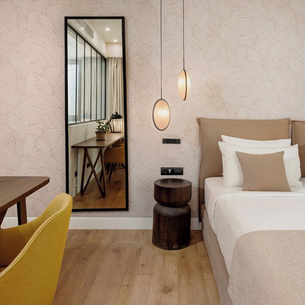 A modern hotel room with a large mirror, a bed with multiple pillows, a small round table, and a yellow chair.