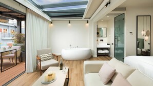 A modern hotel room with a large skylight, a bathtub, a sofa, and a dining area with a table and chairs. - The Residence - Christokopidou Hotel & SPA (Athens)