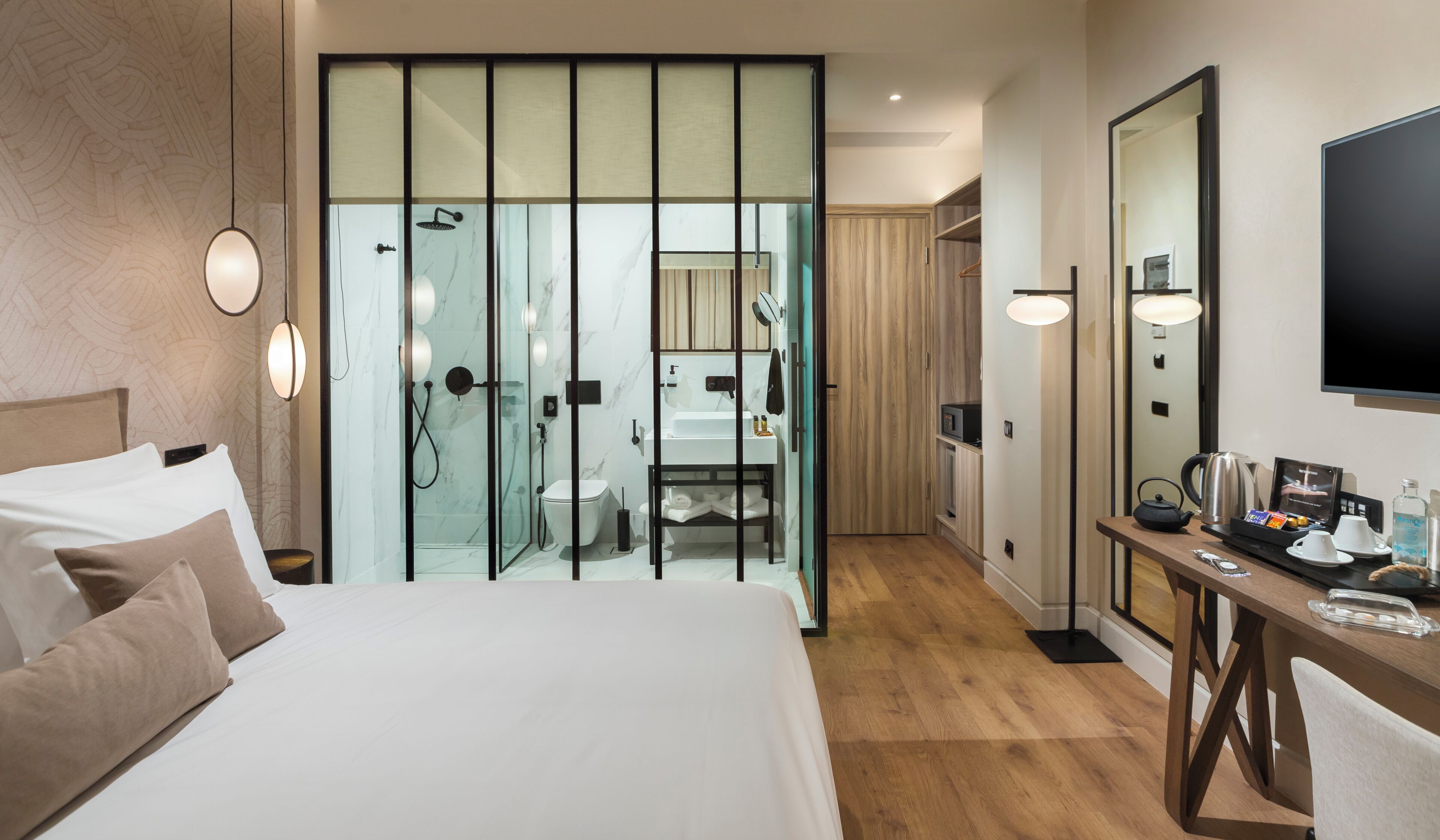 A hotel room with a bed, a bathroom with a shower, a mirror, and a table with amenities.