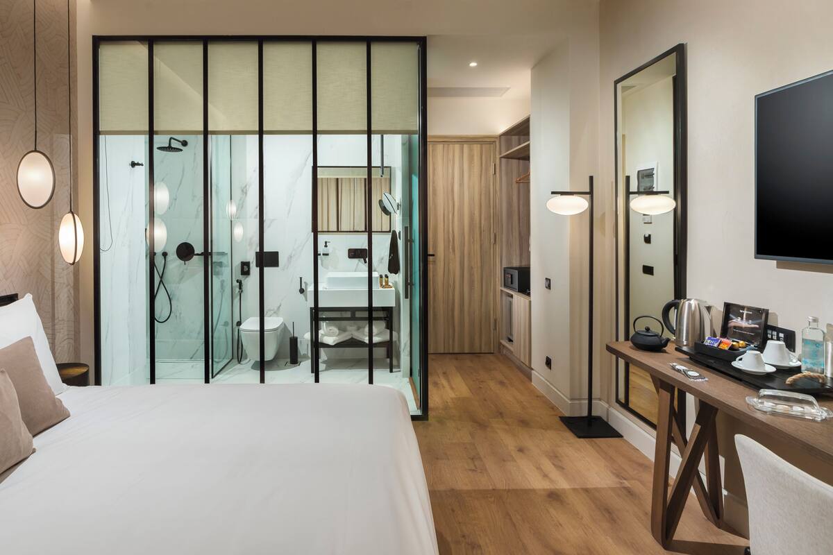 A hotel room with a bed, a bathroom with a shower, a mirror, and a table with amenities.