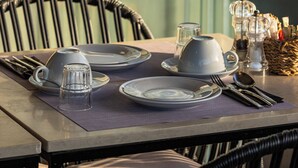 A dining table set with plates, glasses, and cutlery, with a wicker chair in the foreground. - The Residence - Christokopidou Hotel & SPA (Athens)