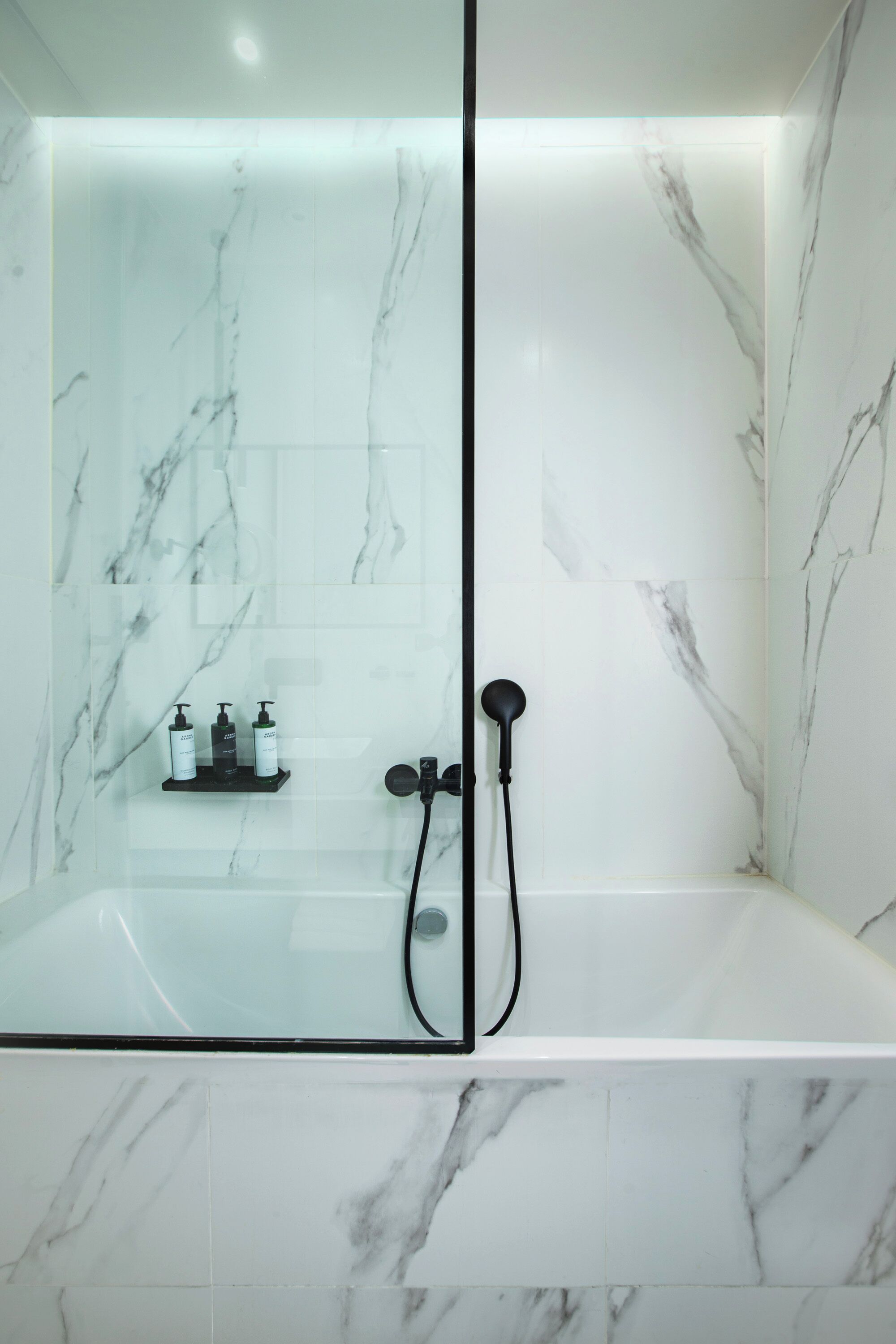Ein modernes Badezimmer mit einer gläsernen Duschkabine und einer Badewanne mit weißen Marmorfliesen.