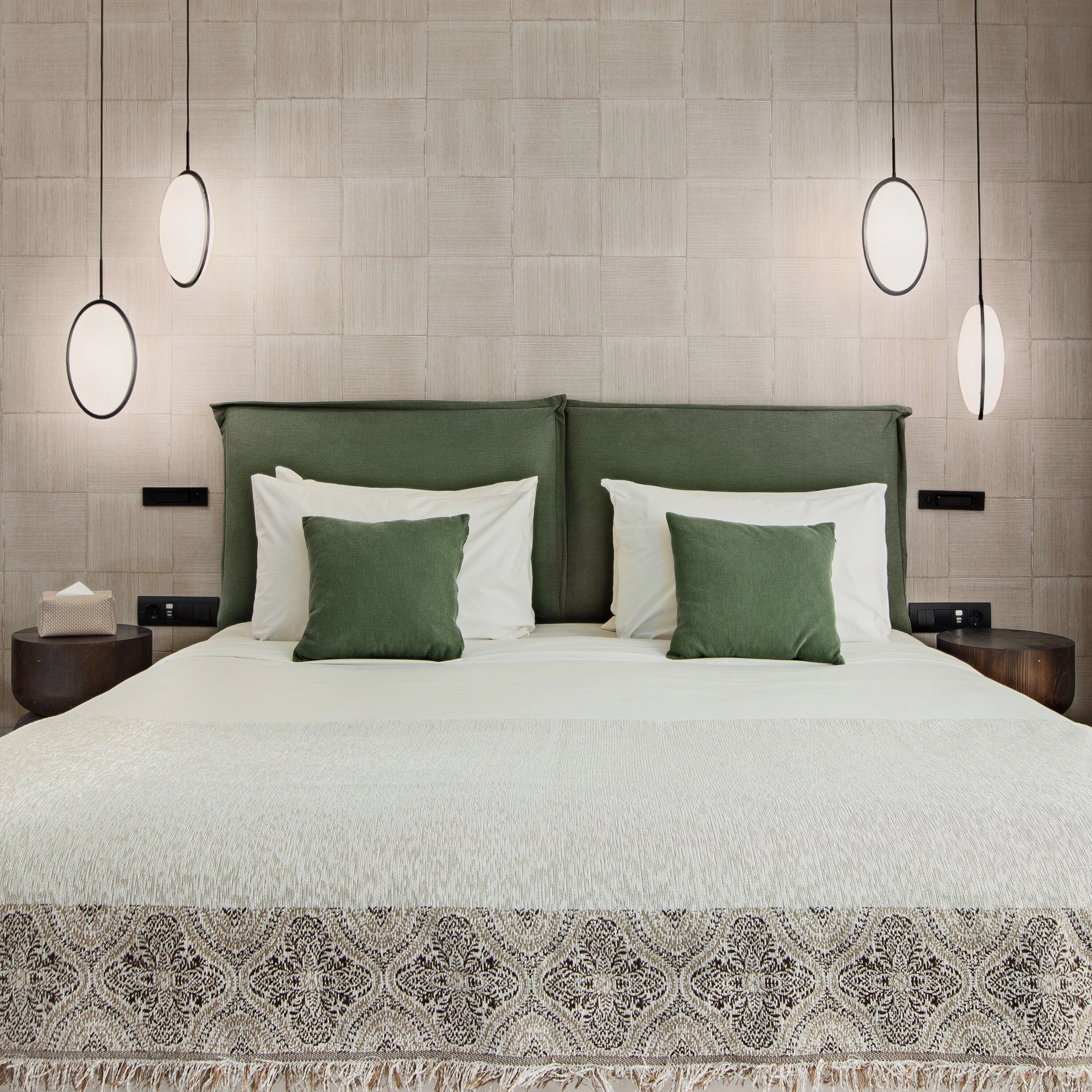 Una cama bien hecha con un cabecero verde, almohadas blancas y un corredor estampado al pie. Hay dos mesitas de noche, con lámparas y una caja de pañuelos sobre una de ellas.