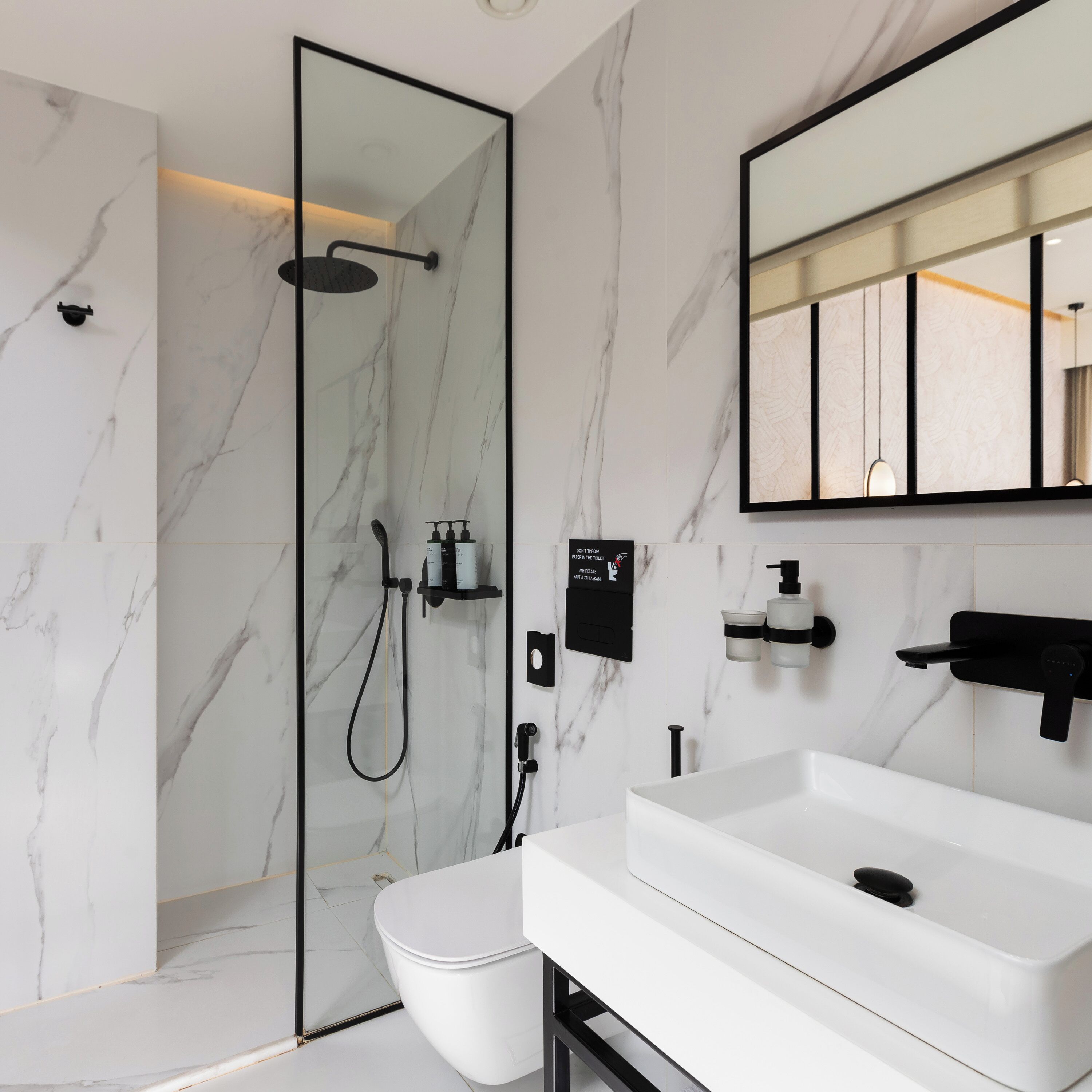 A modern bathroom with a glass-enclosed shower, a white toilet, and a white sink with a black faucet.