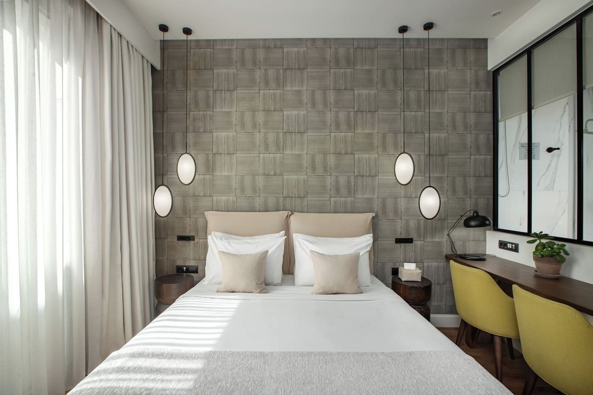 A modern hotel room with a large bed, two bedside tables, a desk with chairs, and a large mirror.