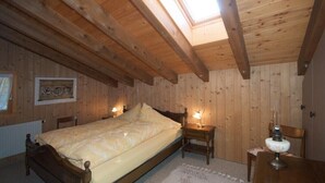 A wooden-paneled bedroom with a skylight, a bed, bedside tables, and a lamp. - Chalet Häsi 3 (4) room attic apartment (Hasliberg-Wasserwendi)